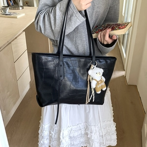 Close-up of black croc-embossed tote bag with cute bear charm and woven tassel detail