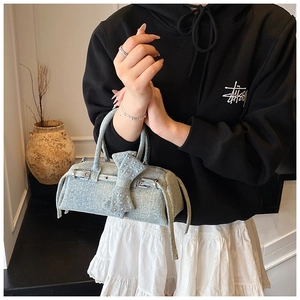 Detail of blue denim baguette bag with large bow, silver studs and Y2K aesthetic