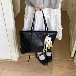 Detail of black crocodile pattern tote bag with bear charm carried by a model