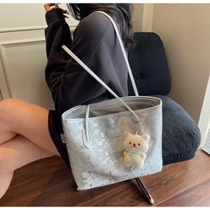 Macro detail of silver tote bag showing metallic texture, letter prints and plush bear