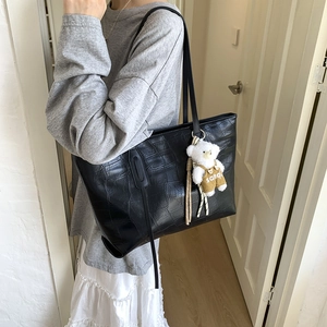 Detail of black croc-effect tote bag with long straps and a cute teddy bear pendant