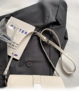 Detail of adjustable metal buckle on a beige minimalist shoulder bag over a grey suit