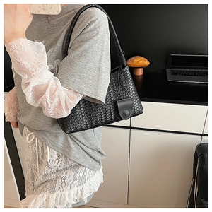 Detail of hand-woven black leather shoulder bag with intricate knot and magnetic flap closure