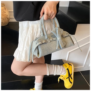 Close-up of light blue denim handbag featuring a large rhinestone bow and metal buckles