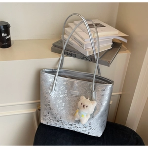 Close-up of silver tote bag featuring digital prints and a cute plush bear pendant