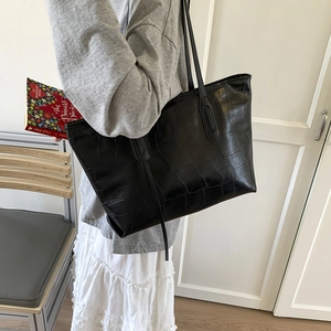 Close-up of black crocodile texture tote bag with slim shoulder straps on a model