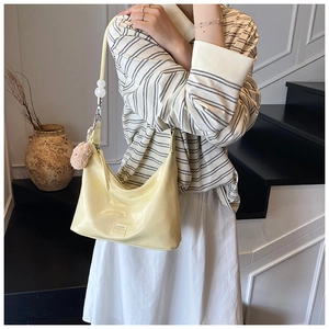 Detail of pale yellow crocodile texture hobo bag with pink pompom and bead strap decoration