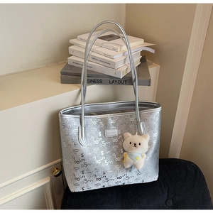 Close-up of metallic silver tote bag with monogram pattern and white bear charm