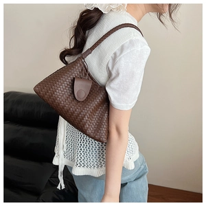 Detail of a brown woven shoulder bag with a crossbody strap shown on a model