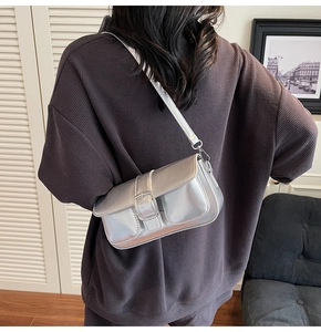 Model wearing a metallic silver crossbody bag with a large buckle in a chic interior setting