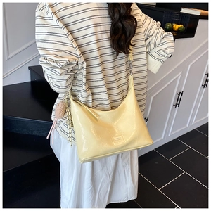 Detail of a creamy yellow crocodile-embossed hobo bag with a plush bear charm pendant