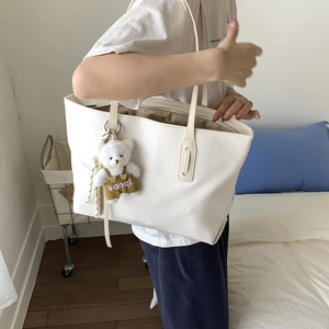 Close-up of a white crocodile embossed tote bag with a cute plush bear charm decoration