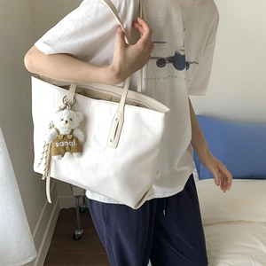 Detail of white crocodile pattern tote bag with a cute plush bear pendant on the strap