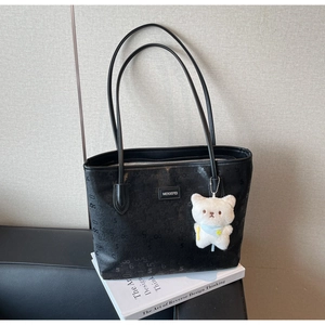 Detail of a black large tote bag with embossed textures and a white plush bear charm
