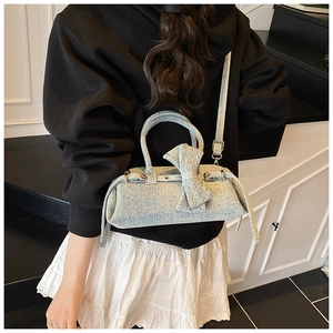 Detail view of light blue denim pillow bag featuring large bow and silver stud accents