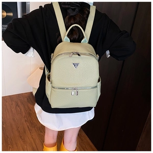 Gros plan d'un sac à dos en cuir vert clair grainé avec logo en métal et bretelles réglables