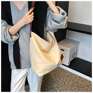 Detail of a large beige canvas tote bag with brown leather straps and corner patch