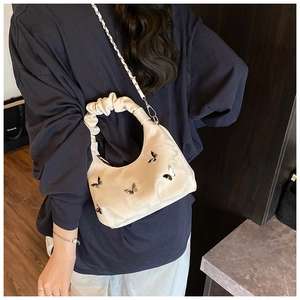 Détail du sac bandoulière crème avec poignée plissée et breloques papillons argentés