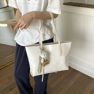 Detail of white crocodile pattern tote bag with teddy bear charm and striped ribbon accent
