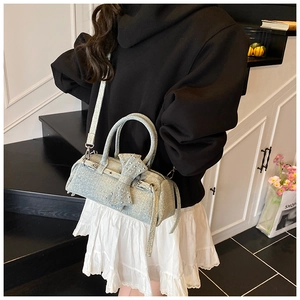 Detail of light blue denim pillow bag featuring rivet bow accents and a cross-body strap