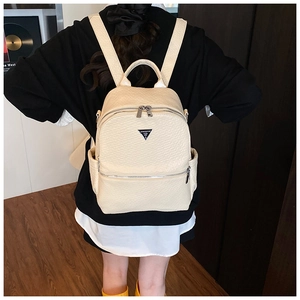 Vue de dos d'une femme portant un sac à dos en similicuir crème avec logo triangulaire
