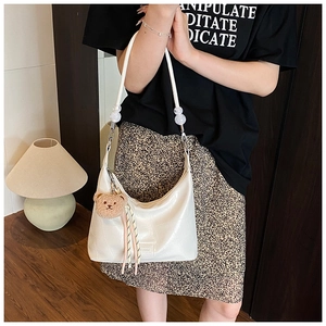 Detailed shot of white faux-crocodile leather crescent bag with bear charm and tassel