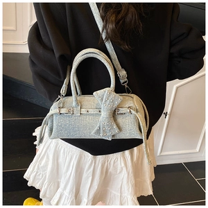 Detail view of light blue denim bow bag with metal rivets and adjustable shoulder strap