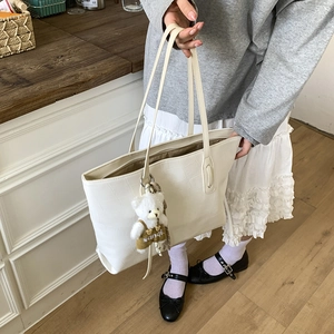 Detail of cream crocodile embossed tote bag with a cute plush bear charm decoration