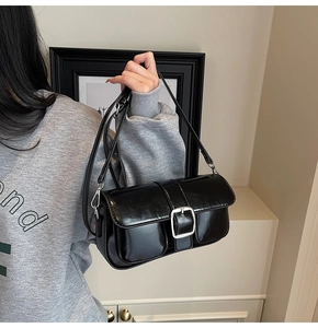 Close-up of stylish black glossy crossbody bag with silver buckle and adjustable strap