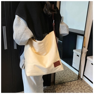 Close-up of off-white canvas tote bag featuring brown wide strap and leather logo patch