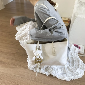Detail of white crocodile texture tote bag with a cute plush bear pendant on long straps