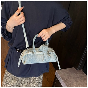 Detail of light blue denim pillow bag featuring a large bow and metallic stud accents