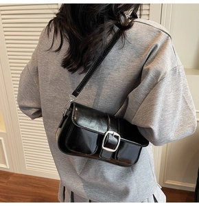 Detail of a black shiny leather crossbody bag with a prominent silver metal square buckle