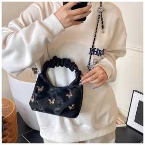 Détail du sac à main plissé noir avec boucles papillon dorées et bandoulière en chaîne