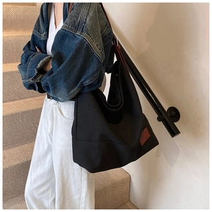Close-up of black canvas tote with brown leather strap and decorative leather patch