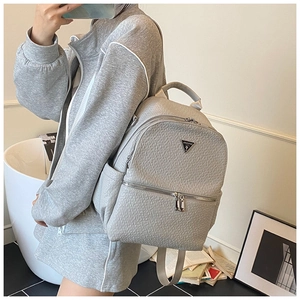 Détail d'un sac à dos gris en similicuir avec texture litchi et logo triangulaire métal