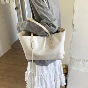 Detail of white crocodile pattern tote bag shown over the shoulder in a minimalist room