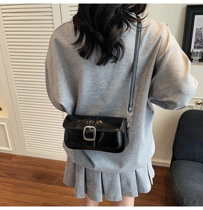 Detail of a shiny black crossbody bag with large silver square buckle and glossy finish