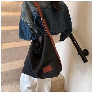 Detail of adjustable brown leather strap and buckle on a black canvas tote bag