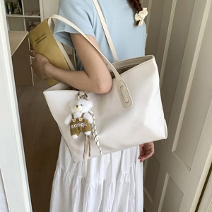 Detail of white crocodile pattern tote bag with a cute bear plush charm on shoulder