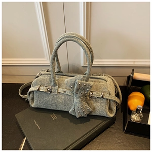 Detail of light blue denim Boston bag featuring a large bow and metallic stud accents