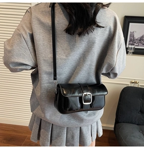 Detail of a black glossy leather crossbody bag with silver buckle worn by a model