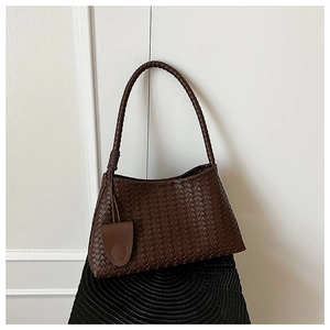 Detailed view of the brown woven leather texture and braided shoulder strap of the bag