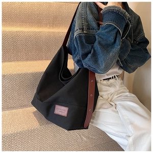 Detail of black canvas hobo bag featuring brown leather strap and brand logo patch