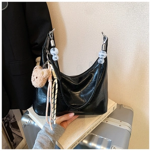 Detail of black crocodile texture hobo bag with teddy bear charm and stylish chain