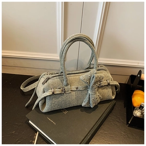 Detail of light blue denim Boston bag featuring a bow and silver buckle on a black book