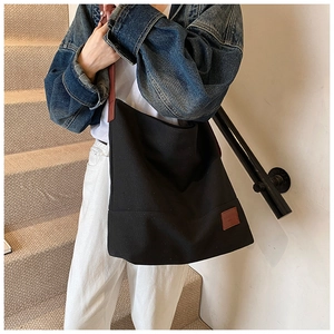 Detail of a large black canvas tote bag with brown straps worn by a model in casual attire