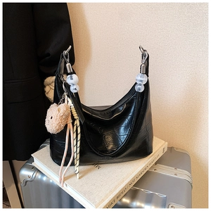 Macro detail of black crocodile pattern leather bag with plush bear charm and handle beads
