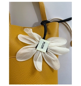 Close-up of yellow pebble leather handbag with a white flower charm and brand tag