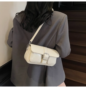 Detail of a chic cream-colored underarm bag with metal buckle and front pocket on model
